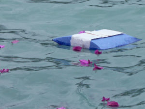 Biodegradable urn floating in water with flower petals