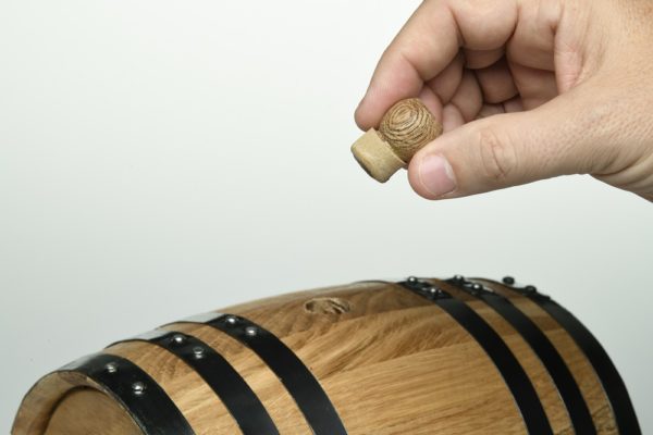 Close up of forever aging wine barrel cremation urn, hand with stopper