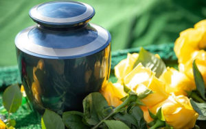 Blue and silver cremation urn with yellow roses on a green background