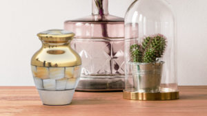 Close up of Mother of Pearl urn next to pink vase and small cactus in a dome on a wooden table